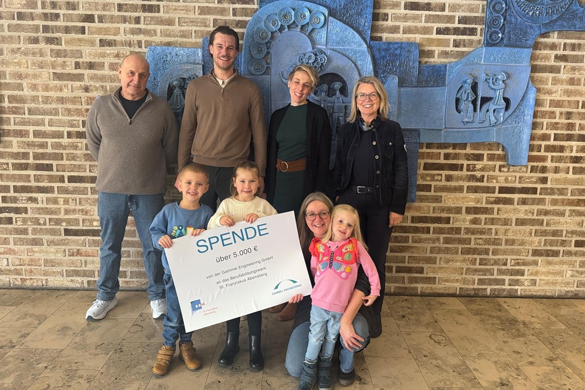 Mike Gammel von Gammel Engineering steh mit dem KIndern und Mitarbeitern des BBW ind er Aula undhält den Scheck in der Hand